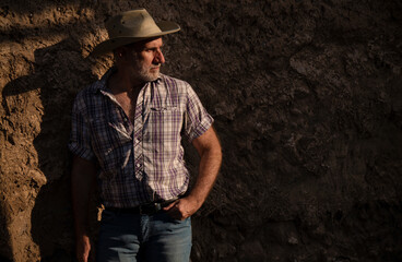 Portrait of adult man in cowboy hat and shirt against abandoned building