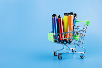 disposable electronic cigarette in a trolley,multicolored vape for smoking in a shopping cart on a blue background,copy space