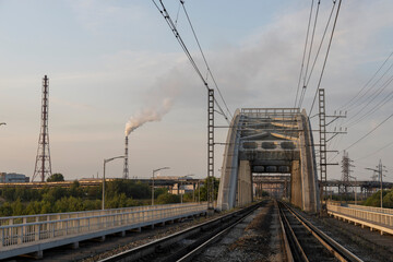 Fototapeta na wymiar Railway bridge against the backdrop of factory pipes.
