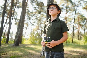 Boy with binoculars. Kid in green forest at summer daytime together.