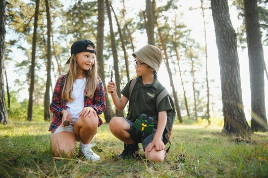 Two Kids In Casual Clothes In Exploring Nature In Forest Together During School Camping Trip With Magnifying Glass.