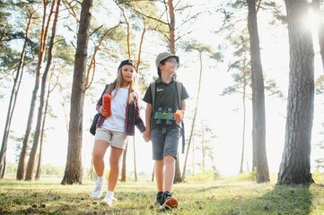 boy and girl go hiking with backpacks on forest road bright sunny day
