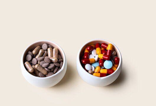 Natural medicine vs conventional medicine concept. Different medical tablets and ayurvedic homeopathy capsules into the white bowl
