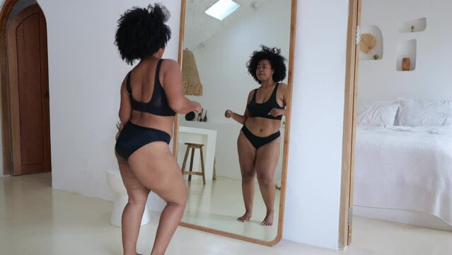 A black female plus size model dances at home in front of a mirror in black lingerie. A woman does not pay attention to excess weight, she loves herself for who she is. Body positive concept.
