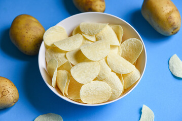 Potato chips snack on bowl, Crispy potato chips on the kitchen table and fresh raw potatoes on blue background