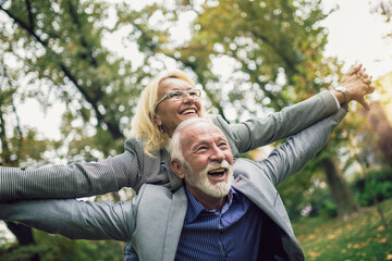 Senior man giving woman piggyback ride through park