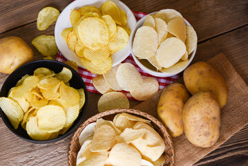 Potato chips snack on bowl and plate, Crispy potato chips on the kitchen table and fresh raw potatoes on wooden background