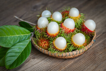 rambutan fruit harvest from the garden rambutan tree, fresh and ripe rambutan sweet tropical fruit peeled rambutan with leaf on wooden basket