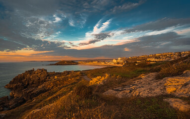 Dramatic sunset in rugged coastal area; town appears in background