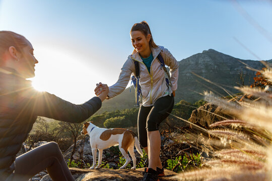 Woman assisting friend in climbing mountain against sky