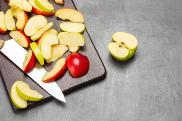 Half a green apple. Slices of green and red apples and kitchen knife on cutting board.