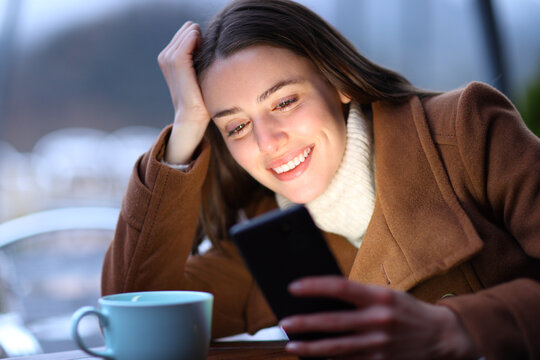 Happy woman checking phone in winter in a coffee shop