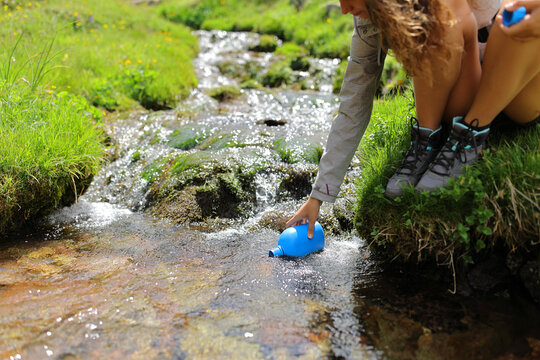 Hiker hand filling canteen of raw water in a creek