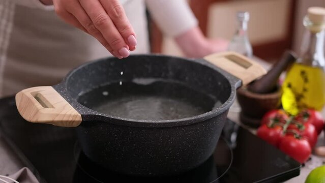 woman adding salt to boiling water in a pot on induction hob at domestic kitchen