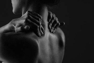 Obraz premium a girl makes herself a massage of her neck with her hands close-up on a dark background, the concept of treatment of the neck and spine