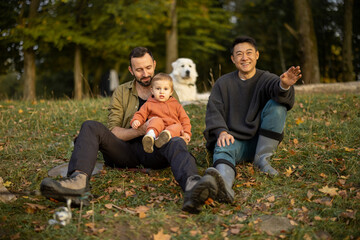Fototapeta premium Multiracial male friends resting and fishing on river or lake coast. Concept of leisure and weekend in nature. Idea of friendship and enjoying time together. Caucasian man with little son. Autumn day