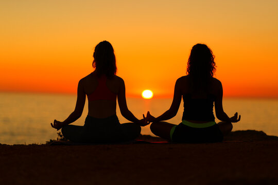 Two women silhouettes doing yoga at sunset