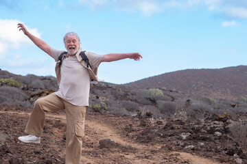 Crazy excited grandparent jumping in outdoors excursion raising one leg with open arms. Senior...