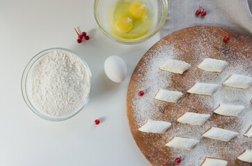 dumplings on a wooden board, next to the ingredients flour, eggs