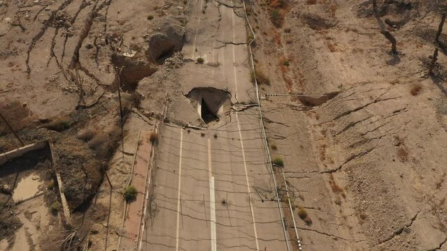 Tilted aerial view of destroyed road in Ein Gedi (Israel), where receding water levels of the Dead Sea lead to sinkholes and craters.

