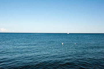 A dark blue sea with a sailboat at the horizon.