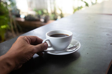 Hand man put black coffe hot coffee on wooden table