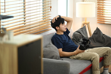 Man in casual clothes resting from playing video game with virtual reality headset, relaxing on couch at home