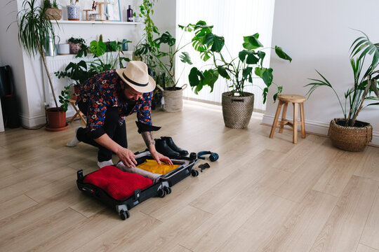 Man wearing hat packing suitcase at home