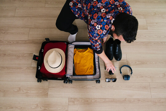 Mature man picking up camera by suitcase on floor at home