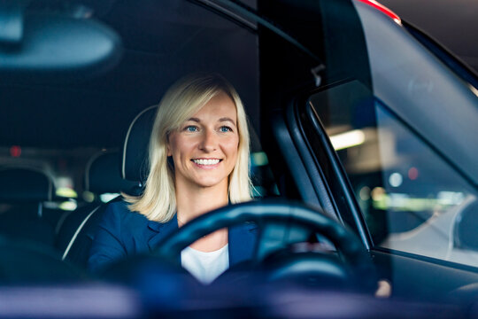 Happy businesswoman with blond hair driving car seen through windshield