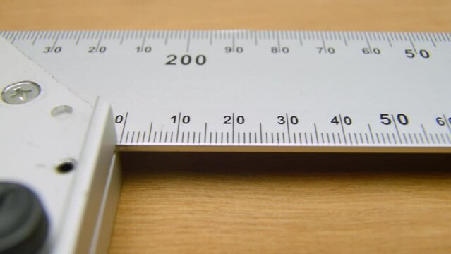 Square angle ruler lying on a table, ready to be used in construction, woodworking. Construction carpenter ruler on a wooden surface L shape straightedge.
 Close up, macro. Wooden surface, background.