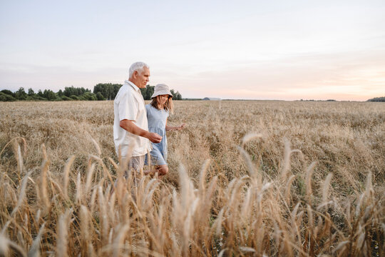 Senior farmer with granddaughter walking in rye field
