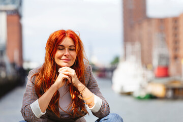 Smiling redhead woman sitting with hands on chin