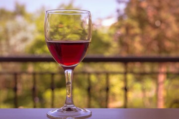 A glass of red wine on a table with a green outdoor background.