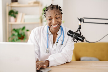 Smiling female doctor with microphone using laptop at home office