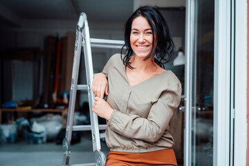 Happy woman leaning on ladder at doorway of home