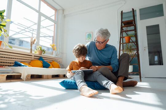 Smiling grandson using tablet computer by grandfather in living room at home