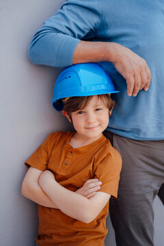 Smiling boy imitating as engineer standing with arms crossed by grandfather in front of wall