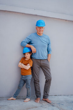Confident grandfather and grandson with hardhat in front of wall