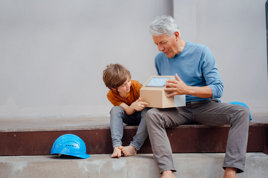 Grandfather examining solar model house with grandson sitting on steps