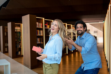 Cheerful man playing with colleague's hair in library