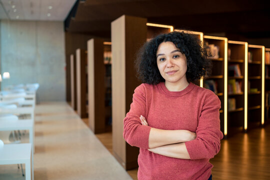 Confident woman with arms crossed in illuminated library