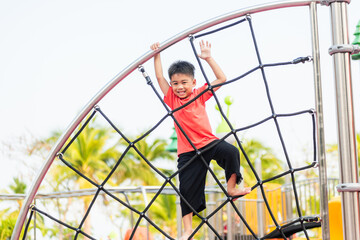 Asian child smiling playing climbing outdoor playground, happy preschool little kid having funny while playing climbs on a rope climbing net on playground equipment in daytime in summer, Little boy