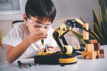 Happy Asian little kid boy using screwdriver to fixes screws robotic machine arm in home workshop,...