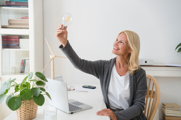 Happy freelancer with light bulb sitting at desk in home office