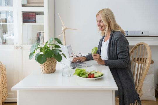 Happy freelancer with aptop eating healthy snack at home office