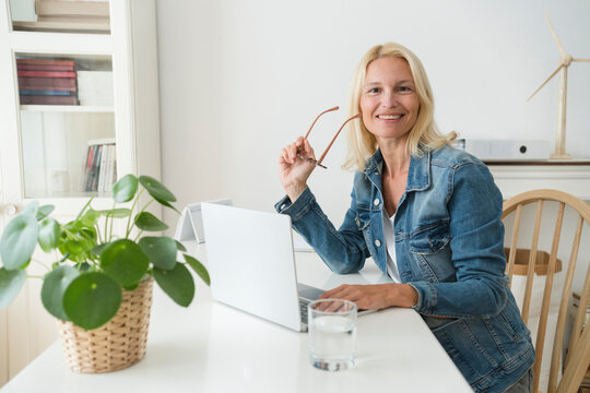 Smiling freelancer with eyeglasses sitting at desk in home office