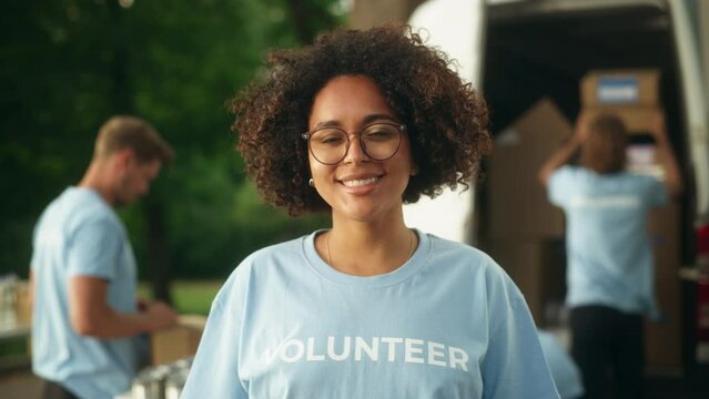 Portrait of a Happy Helpful Black Female Volunteer. Young Adult Multiethnic Latina with Afro Hair, Wearing Glasses, Smiling, Posing for Camera. Humanitarian Aid and Volunteering Concept.