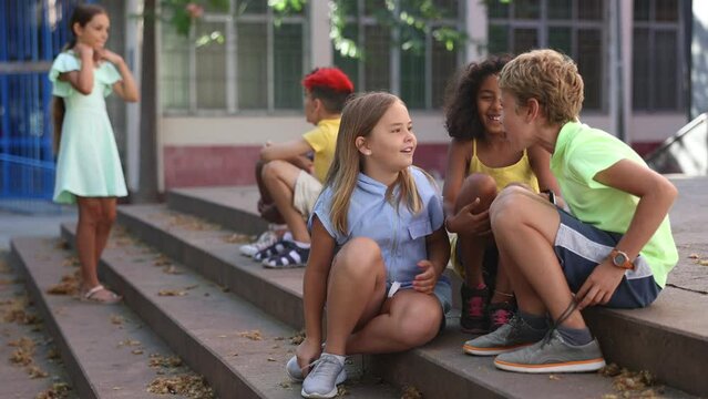 Group of multiracial boys and girls sitting on stairs outdoors and having conversation. 