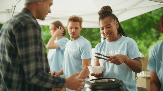 Humanitarian Aid Concept: Volunteers Preparing Free Food and Feeding Local Community that is in Need. Charity Workers Serve Noodles and Fruits to Hungry Homeless People.